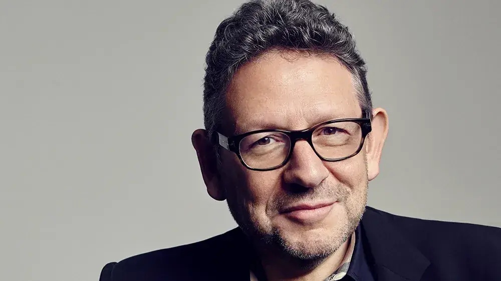 Portret van Sir Lucian Grainge, topman van Universal Music Group, met bril tegen een grijze achtergrond