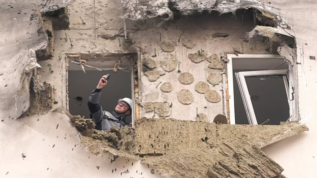 Een hulpverlener met helm inspecteert een compleet weggeslagen gevel van een woning na een droneaanval