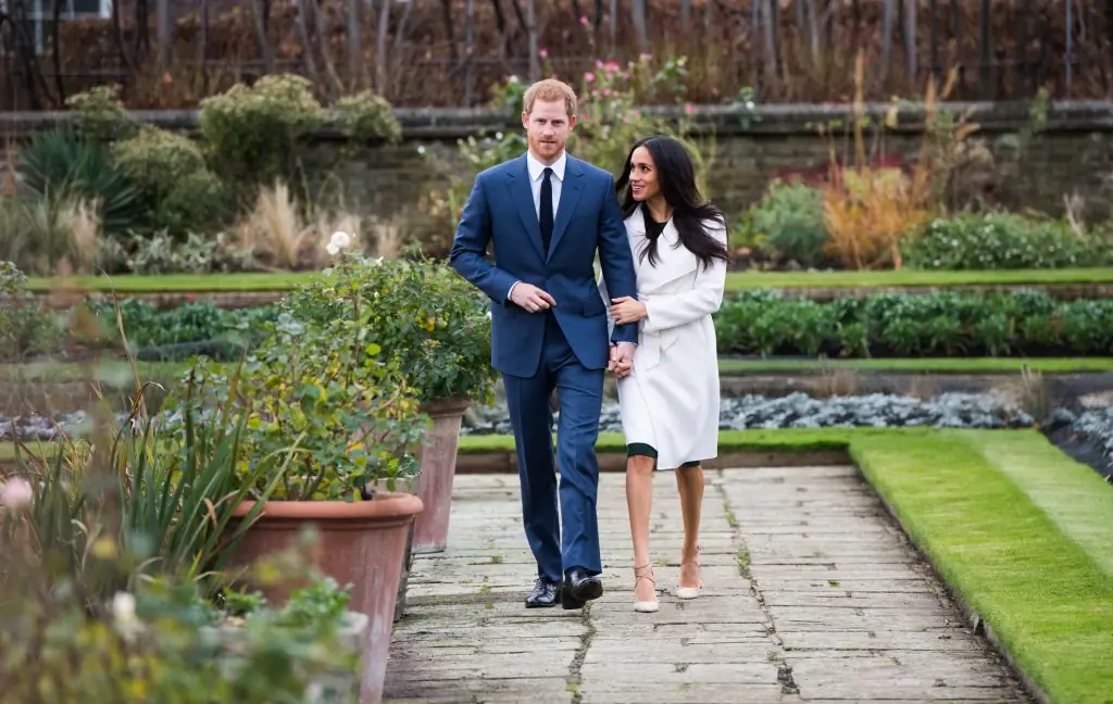 Prins Harry in blauw pak en Meghan Markle in witte jas lopen gearmd over een tuinpad