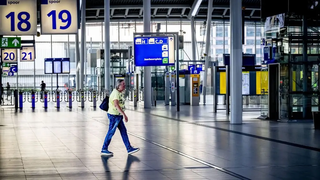 Een vrouw loopt alleen door de vrijwel lege stationshal van Utrecht Centraal, langs gesloten poortjes en borden voor spoor 18 en 19