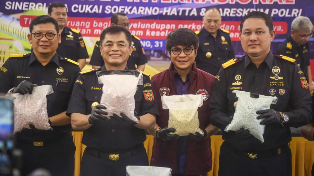 Indonesische douanebeambten in zwarte uniformen tonen op een persconferentie doorzichtige zakken met duizenden pillen