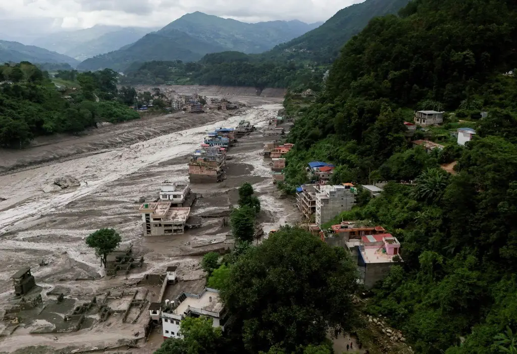 Luchtfoto van een dal in Nepal waar een brede modderstroom huizen aan de rivieroever heeft weggeslagen