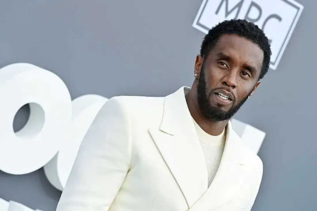 Sean Combs in een crème kleurig pak kijkt in de camera op een rode loper