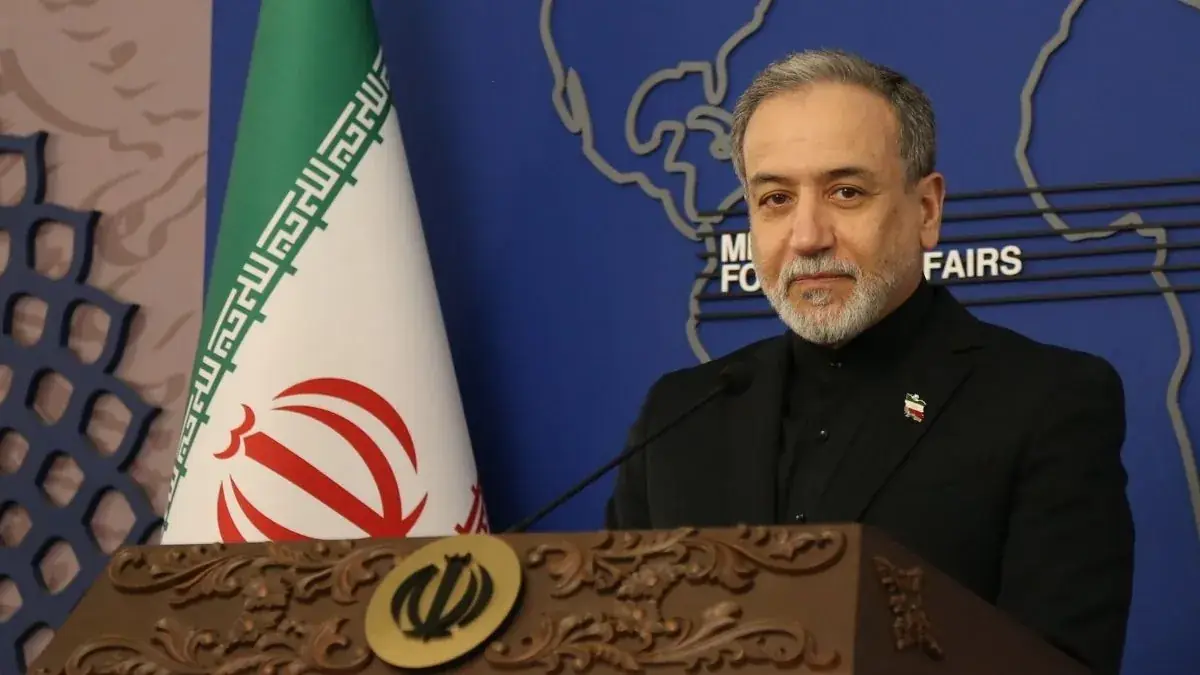De Iraanse minister van Buitenlandse Zaken Abbas Araghchi staat achter een houten spreekgestoelte, met naast zich de Iraanse vlag en achter zich een wereldkaart met de tekst Ministry of Foreign Affairs