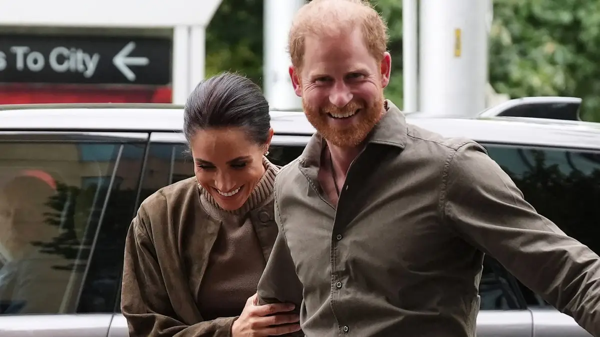 Prins Harry en Meghan Markle lopen lachend gearmd langs een auto bij een aankomst