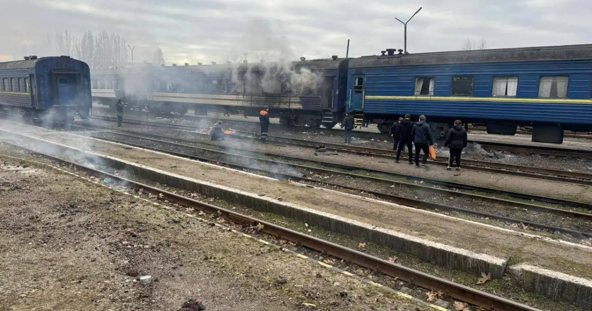 Rook stijgt op tussen beschadigde treinstellen op een station, met mensen die de schade bekijken