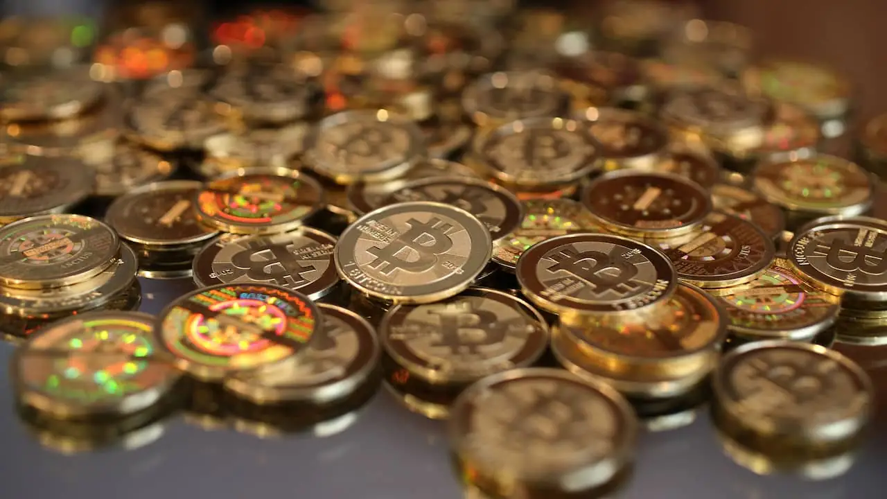 Tientallen goudkleurige munten met het bitcoinlogo liggen door elkaar op een tafel, met de voorste munt scherp in beeld