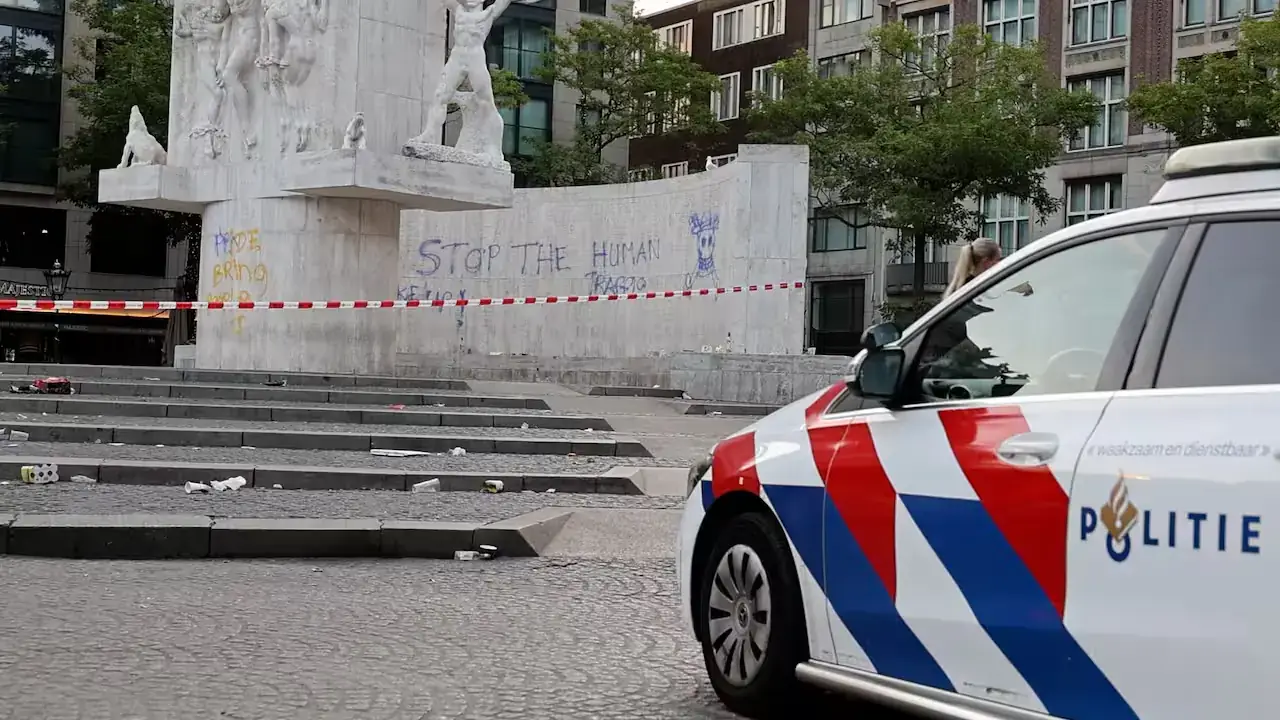 Een politieauto staat op de Dam voor het met lint afgezette Nationaal Monument, met daarop de blauwe graffititekst Stop the human traffic en een doodskop