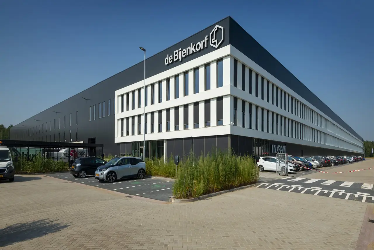 Het distributiecentrum van de Bijenkorf met het logo op de gevel en geparkeerde auto's ervoor