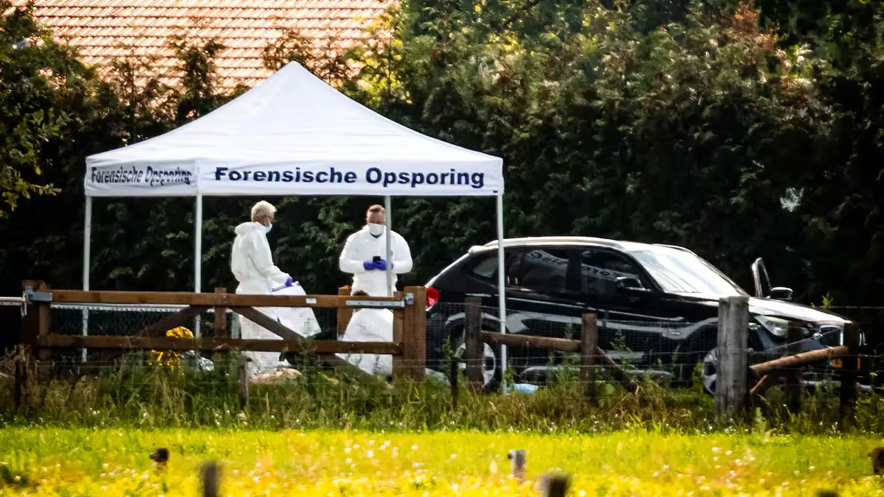 Twee rechercheurs in witte overalls onder een tent van de Forensische Opsporing achter een houten hek bij een woning in het buitengebied