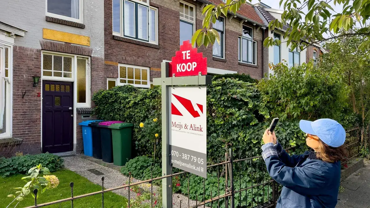 Voorbijganger fotografeert een Te Koop-bord van een makelaar voor een rij oude woningen