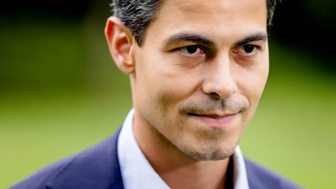 Close-up portret van premier Rob Jetten in pak, met een lichte glimlach en een groene, onscherpe achtergrond