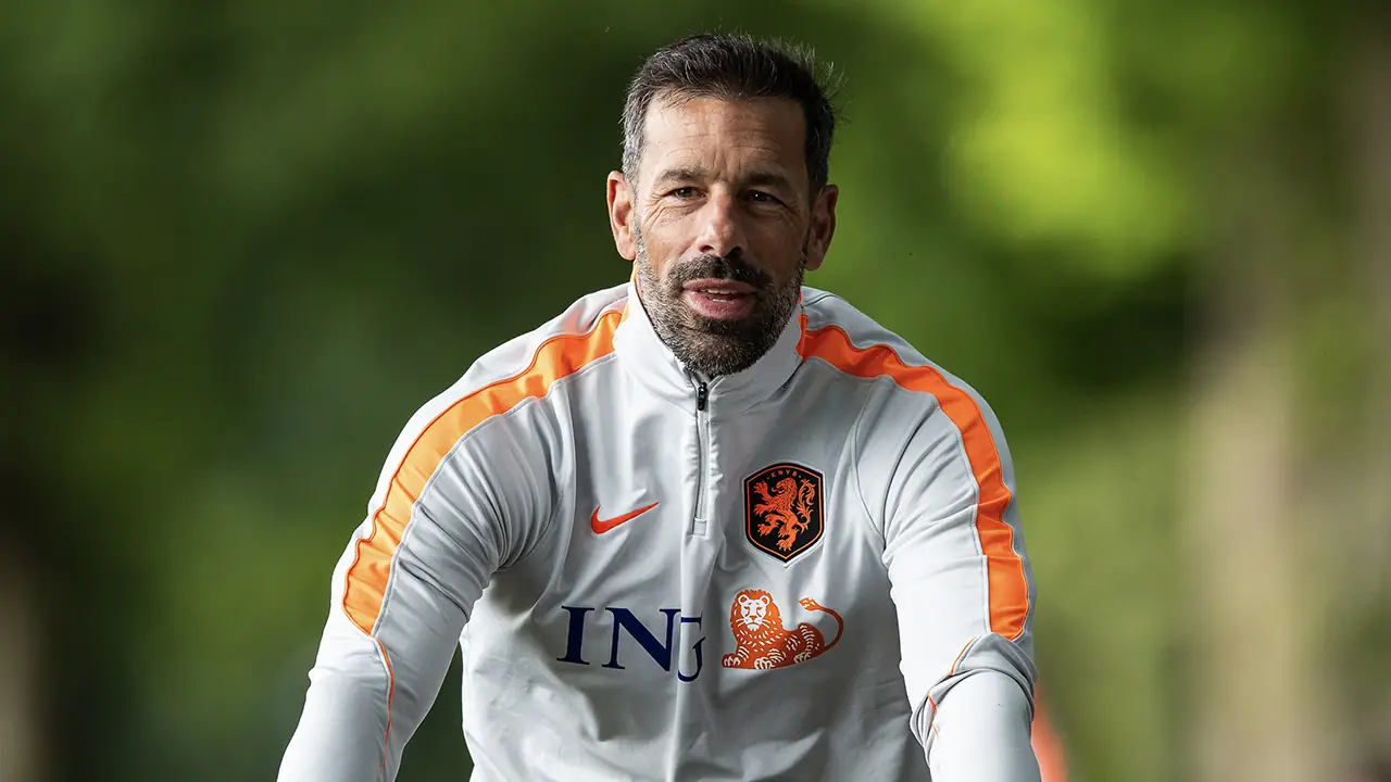 Ruud van Nistelrooij in een wit trainingsjack met het KNVB-logo en oranje strepen op een trainingsveld
