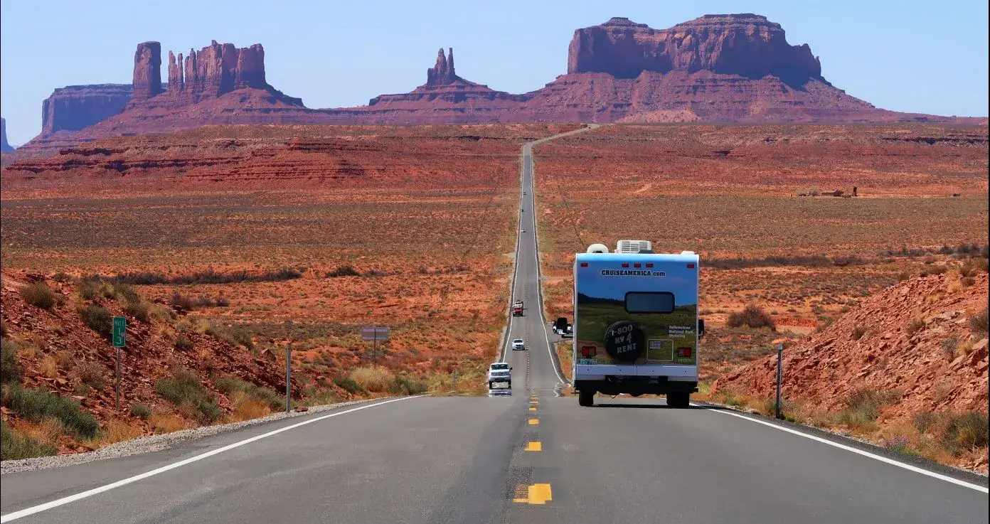 Een witte huurcamper rijdt over de kaarsrechte snelweg 163 richting de rode rotsformaties van Monument Valley