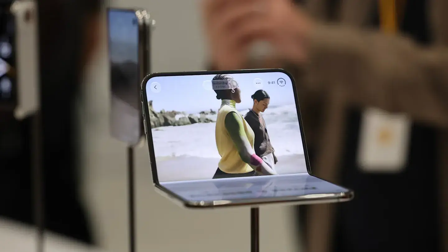 De iPhone Duo opengevouwen op een display-standaard, met wazige bezoekers op de achtergrond