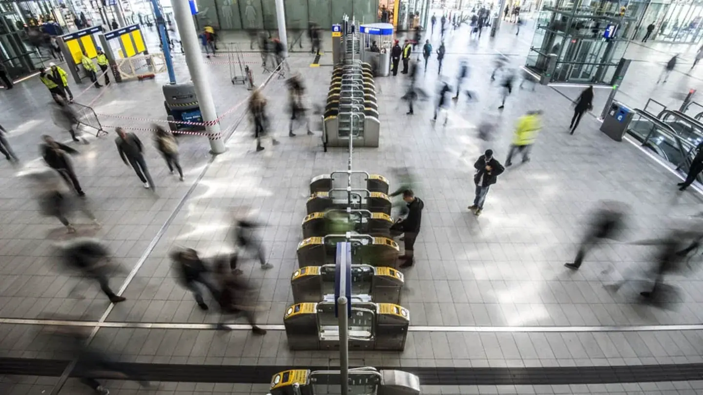 Wazige, in beweging vastgelegde reizigers haasten zich door een drukke stationshal langs incheckpoortjes