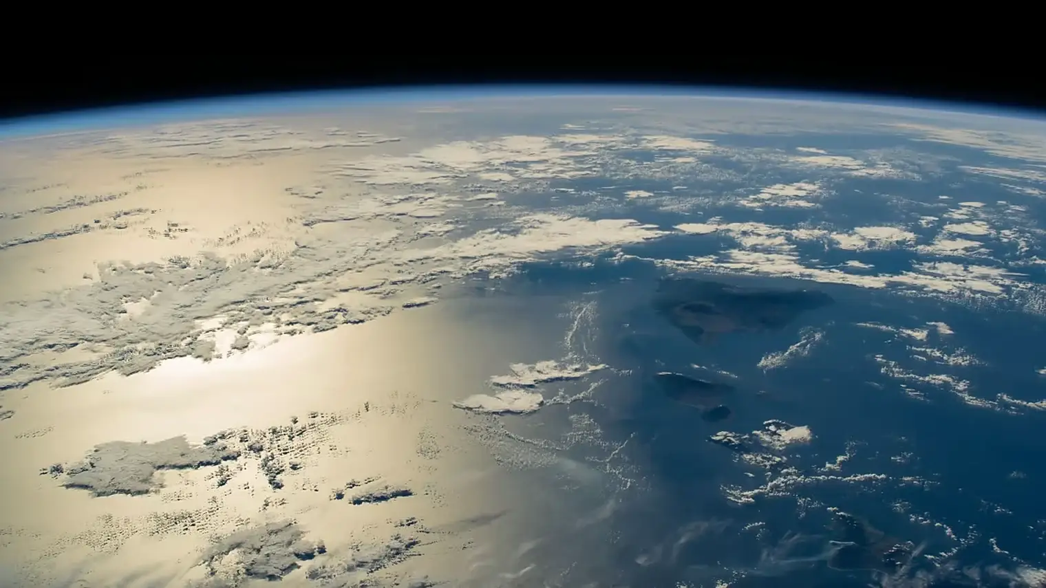 De aarde vanuit een baan, met de gebogen horizon, wolkenvelden, zonlicht dat weerkaatst op de oceaan en enkele eilanden onder een zwarte hemel