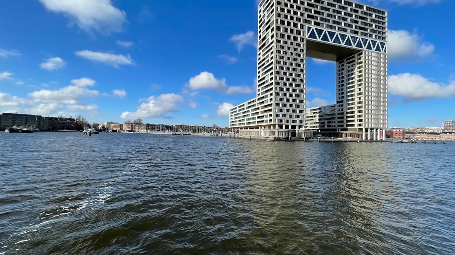 Het IJ in Amsterdam met golvend water op de voorgrond en een gebouw met een grote doorgang aan de waterkant