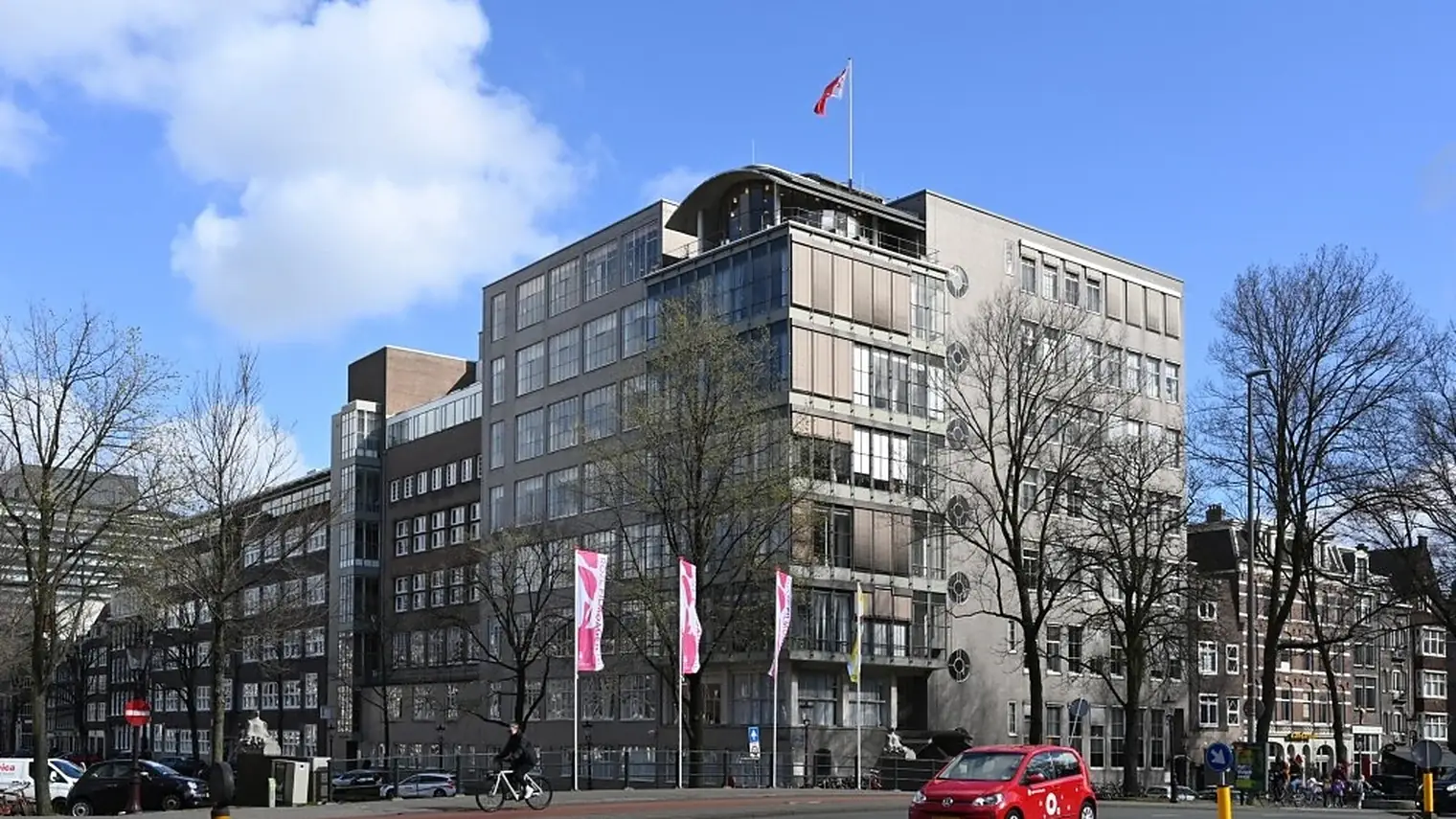 Het hoofdkantoor van de GGD Amsterdam, een hoog kantoorgebouw op een hoek met vlaggen ervoor