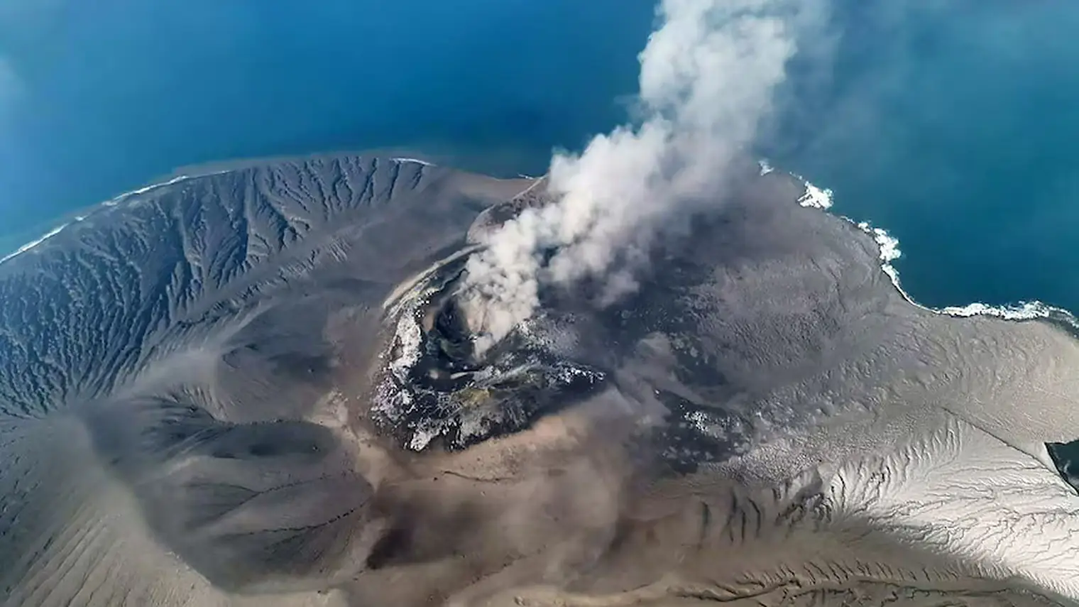 Luchtfoto van de vulkaan Anak Krakatau met een aswolk die uit de krater opstijgt, omringd door zee