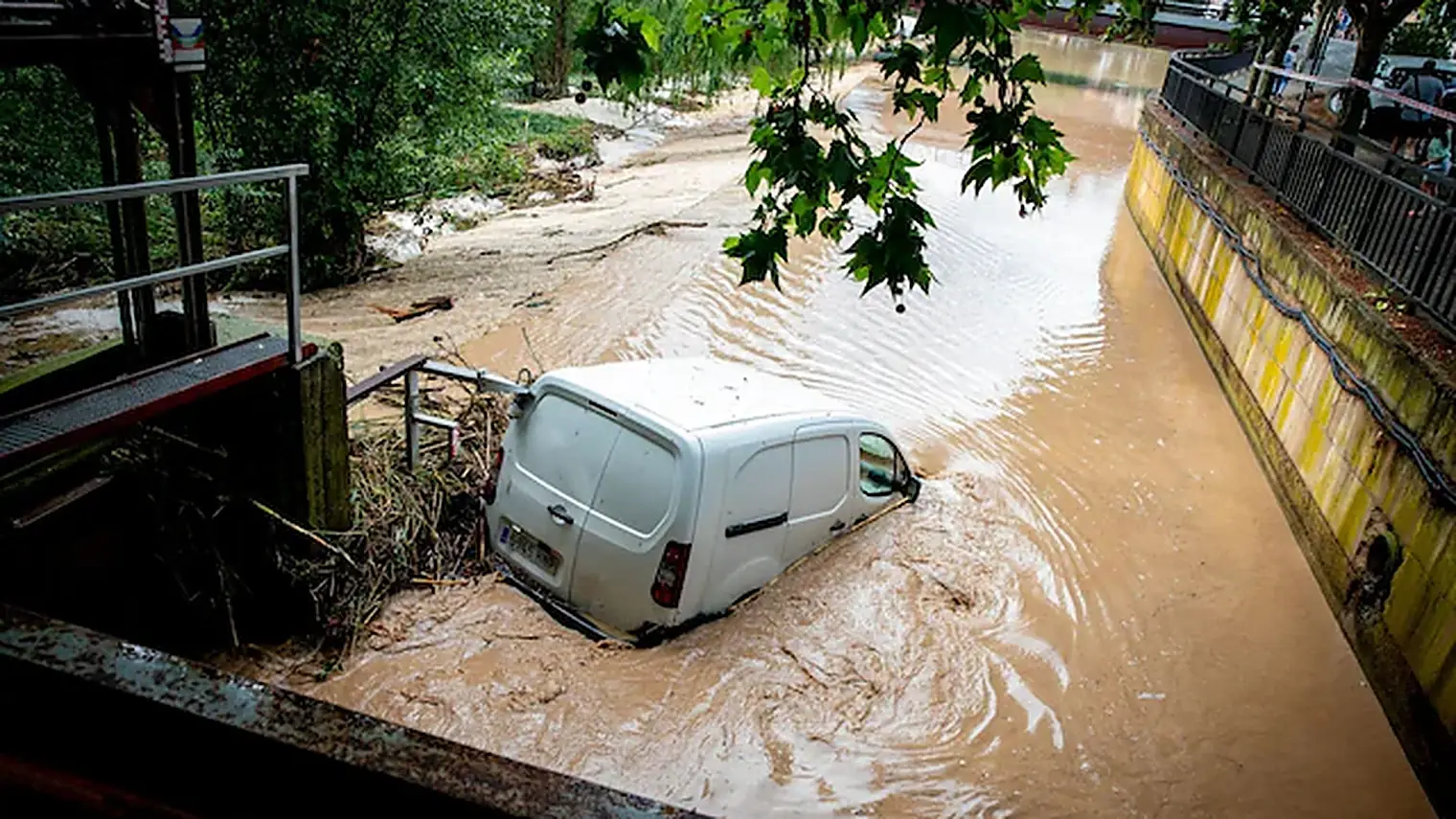 Een witte bestelbus staat half onder in het bruine water van een overstroomde rivierbedding