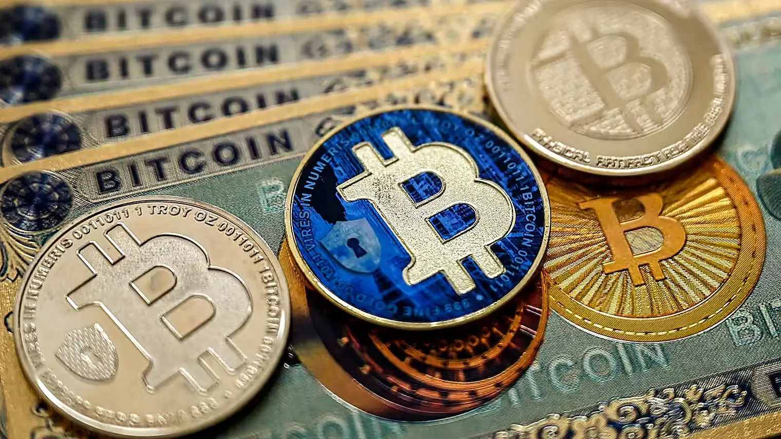 Verschillende bitcoinmunten in goud en blauw liggen op bankbiljetten met de tekst Bitcoin