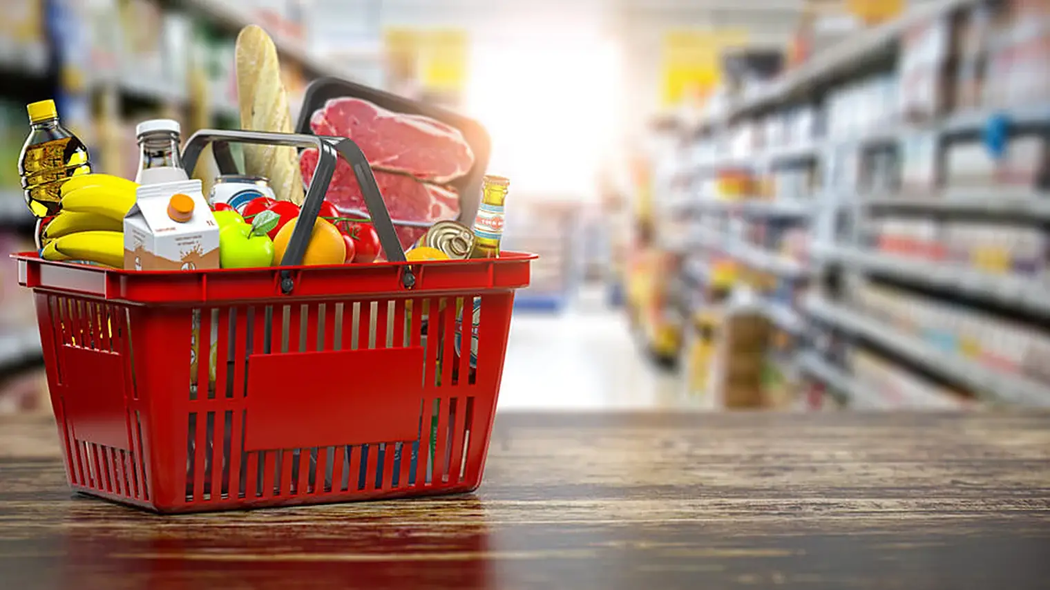 Rood boodschappenmandje met brood, vlees, fruit en zuivel op een houten blad in een supermarktgangpad