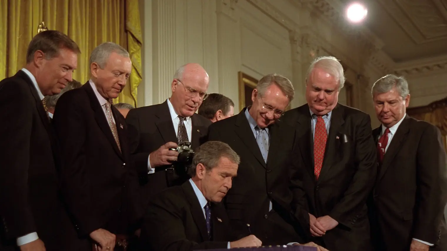 President George W. Bush ondertekent de Patriot Act aan een bureau in de East Room van het Witte Huis, omringd door senatoren en Congresleden