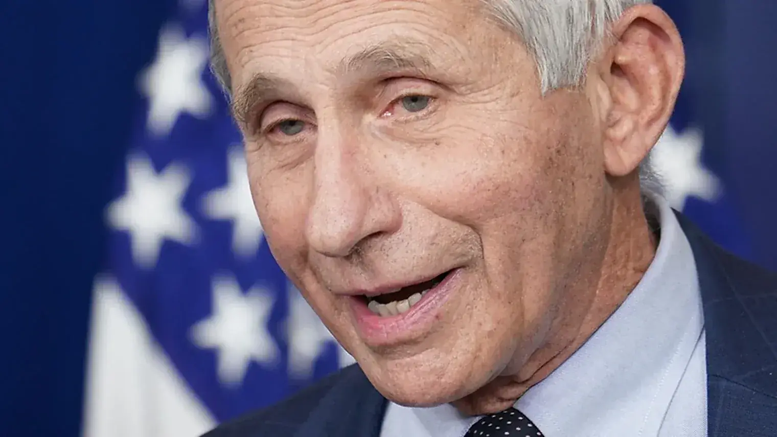 Anthony Fauci in close-up voor een Amerikaanse vlag, pratend tijdens een persmoment
