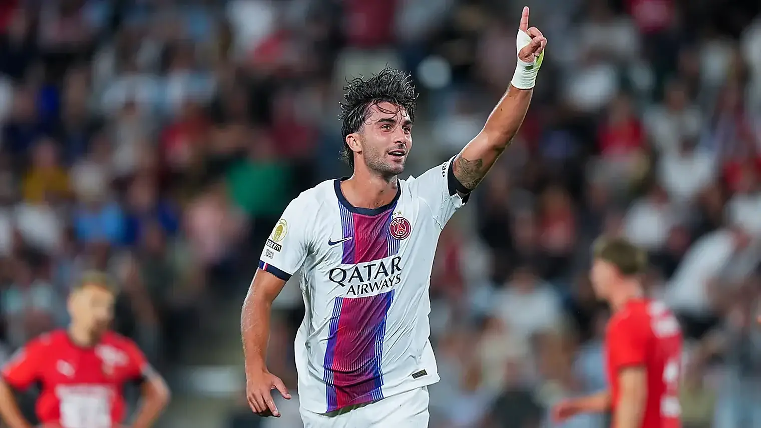 Ferran Torres in het witte uitshirt van Paris Saint-Germain steekt na een doelpunt zijn wijsvinger omhoog, met spelers van Rennes in het rood op de achtergrond
