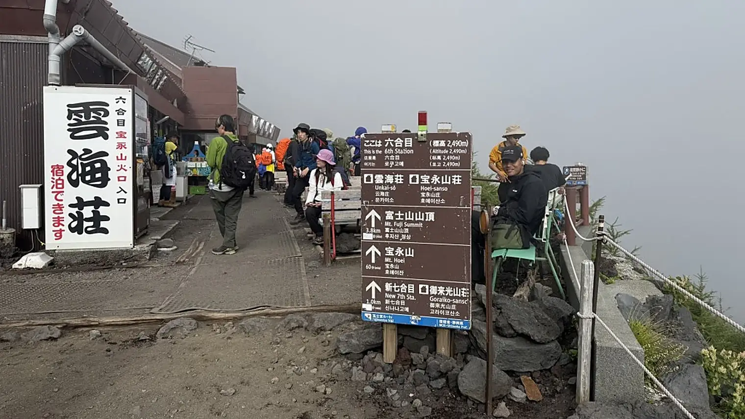 Het zesde station op Fuji met een bord dat 2.490 meter hoogte aangeeft, wandelaars op bankjes en een berghut in de mist