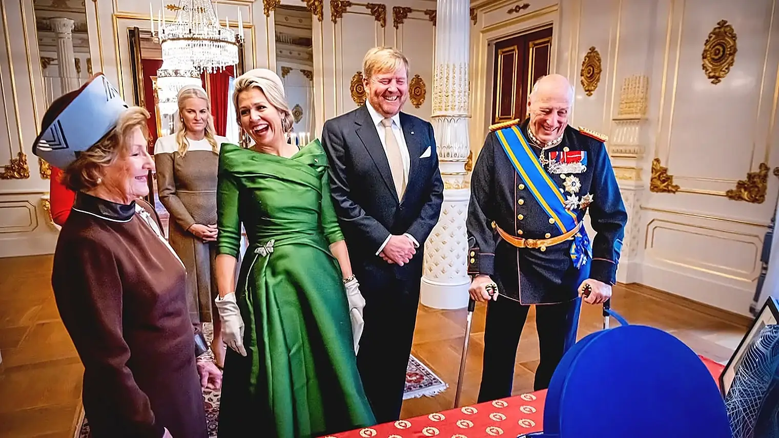Koning Harald met een wandelstok lacht in uniform naast koning Willem-Alexander, koningin Maxima in een groene jurk, koningin Sonja en kroonprinses Mette-Marit in een zaal van het paleis in Oslo
