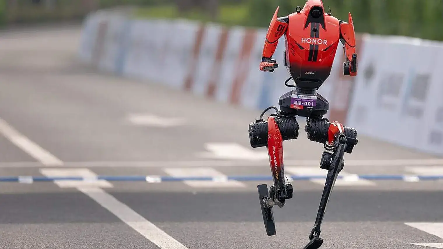 Rode robot van Honor met het opschrift Flash op het bovenbeen rent over asfalt langs afzethekken