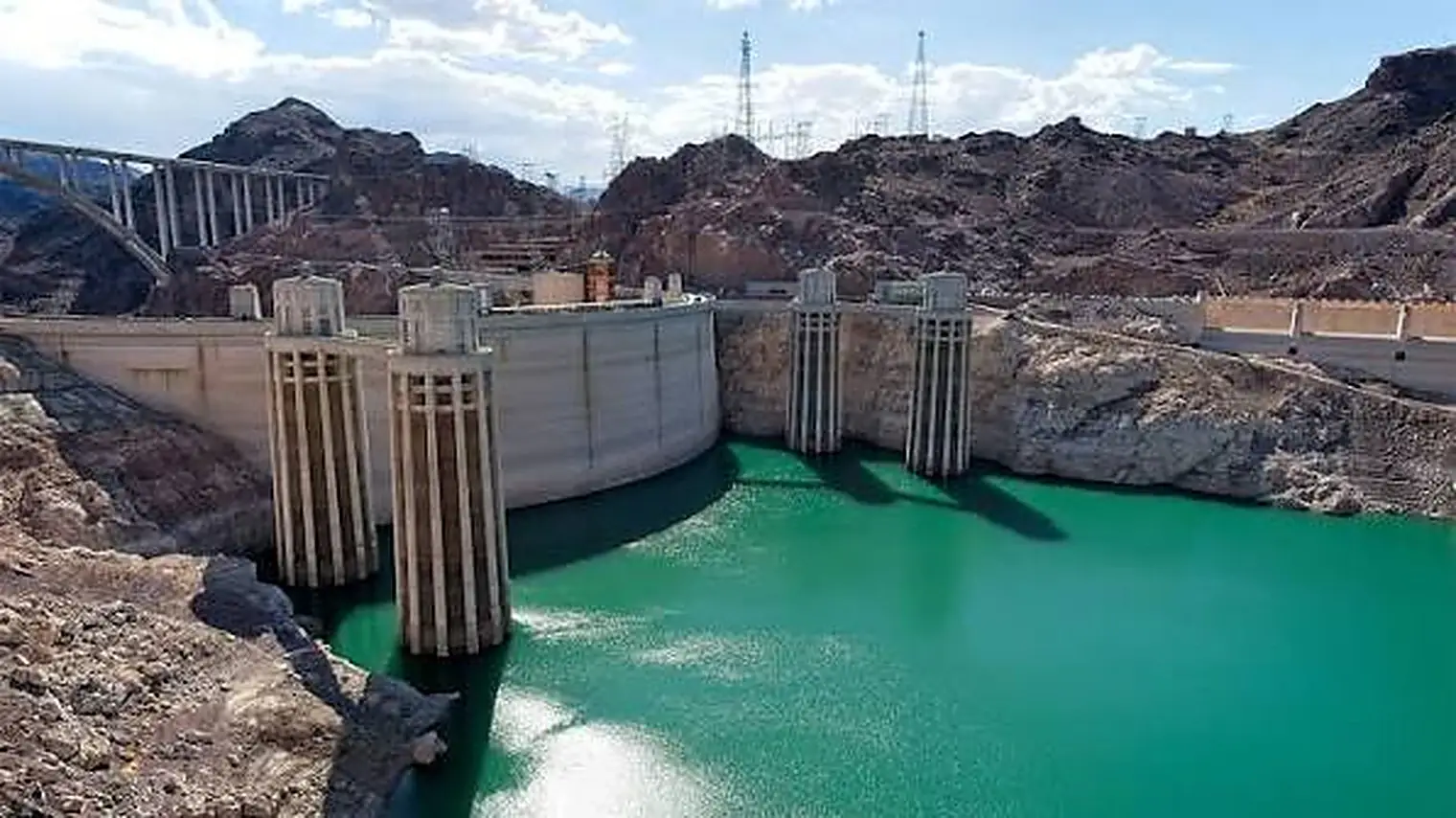De Hoover Dam met de inlaattorens boven een laag turquoise waterpeil, met witte kalkaanslag op de rotswanden