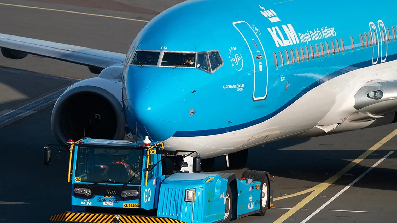 Neus van een blauw-witte KLM Boeing met een sleepvoertuig ervoor op het platform van Schiphol