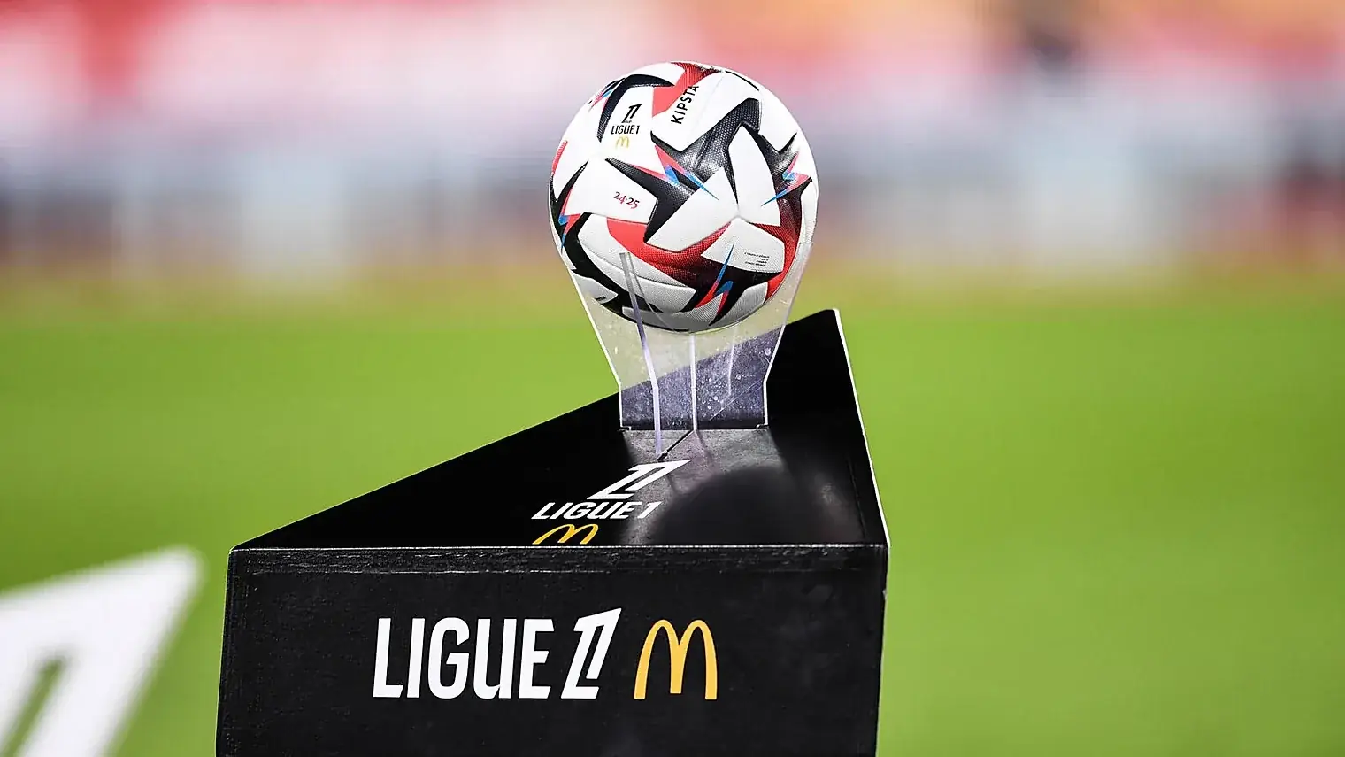 De wedstrijdbal van de Ligue 1 op een zwarte zuil met het competitielogo, met een onscherp stadion op de achtergrond