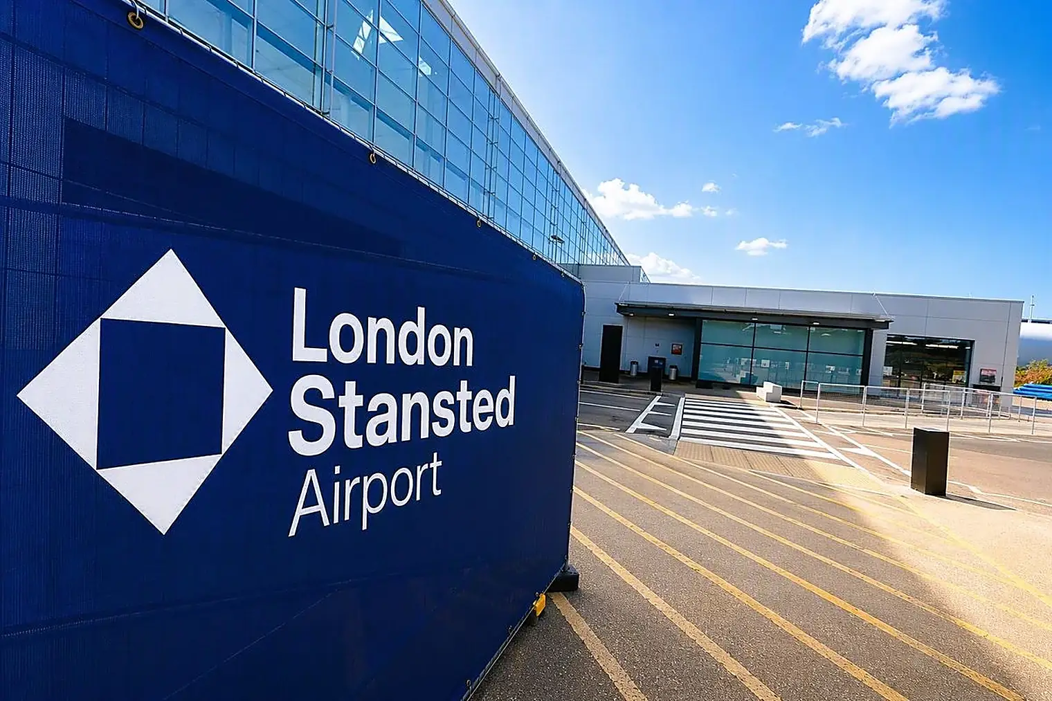 Groot blauw bord met het logo van London Stansted Airport voor de terminal, onder een blauwe lucht