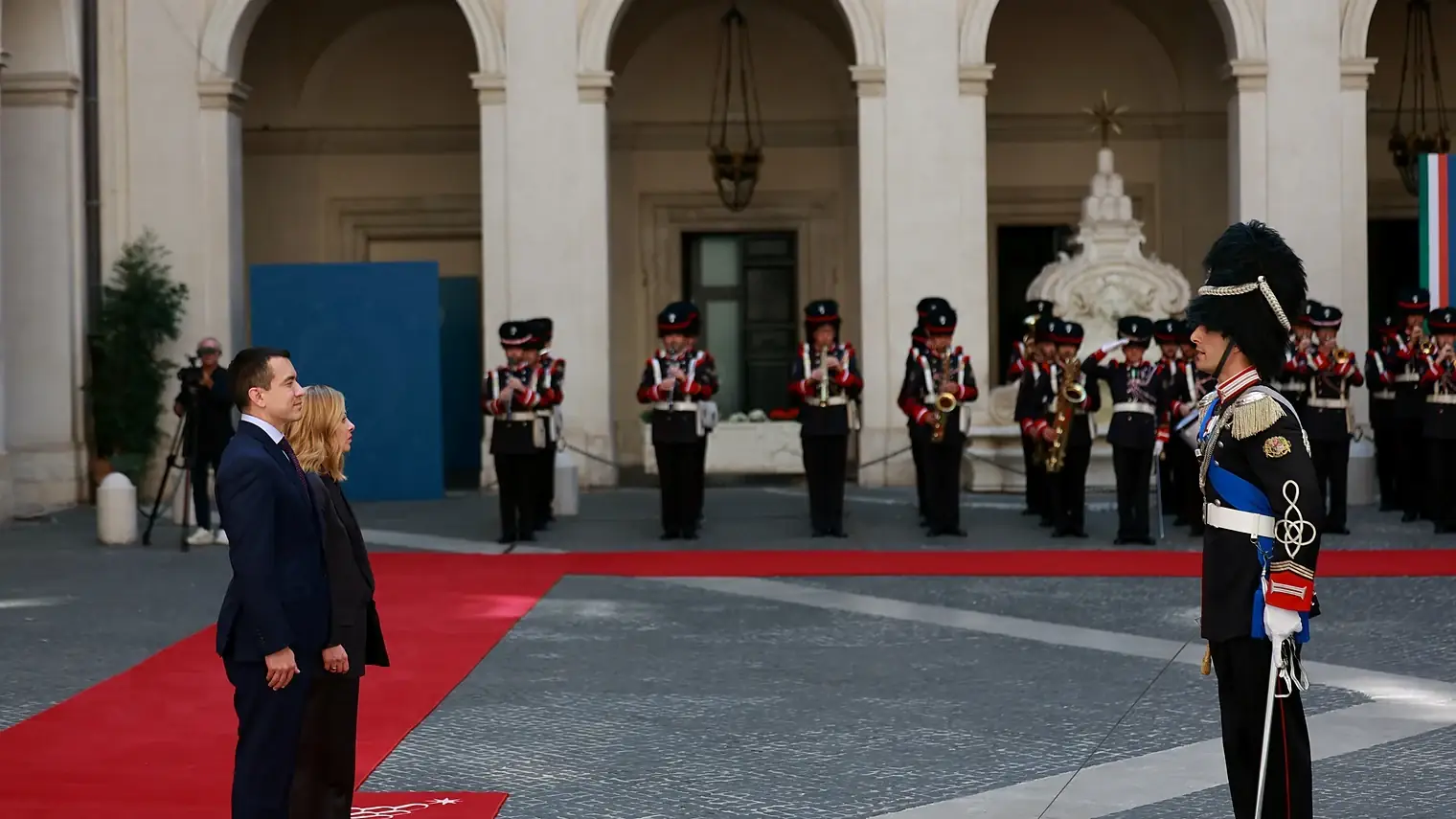 Meloni staat met een gast op een rode loper op de binnenplaats van Palazzo Chigi, met een erewacht en een militaire kapel op de achtergrond