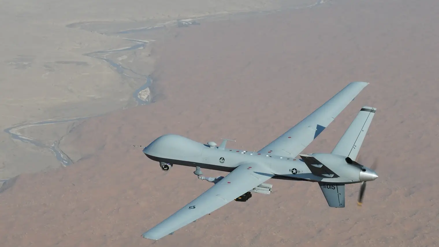Een Amerikaanse MQ-9 Reaper-drone in een scherpe bocht boven een droog woestijnlandschap
