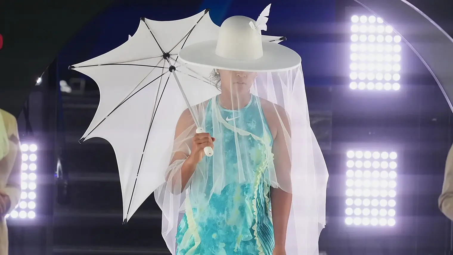 Osaka onder een witte parasol, met een brede witte hoed met sluier en een turquoise jurk met golvende ruches