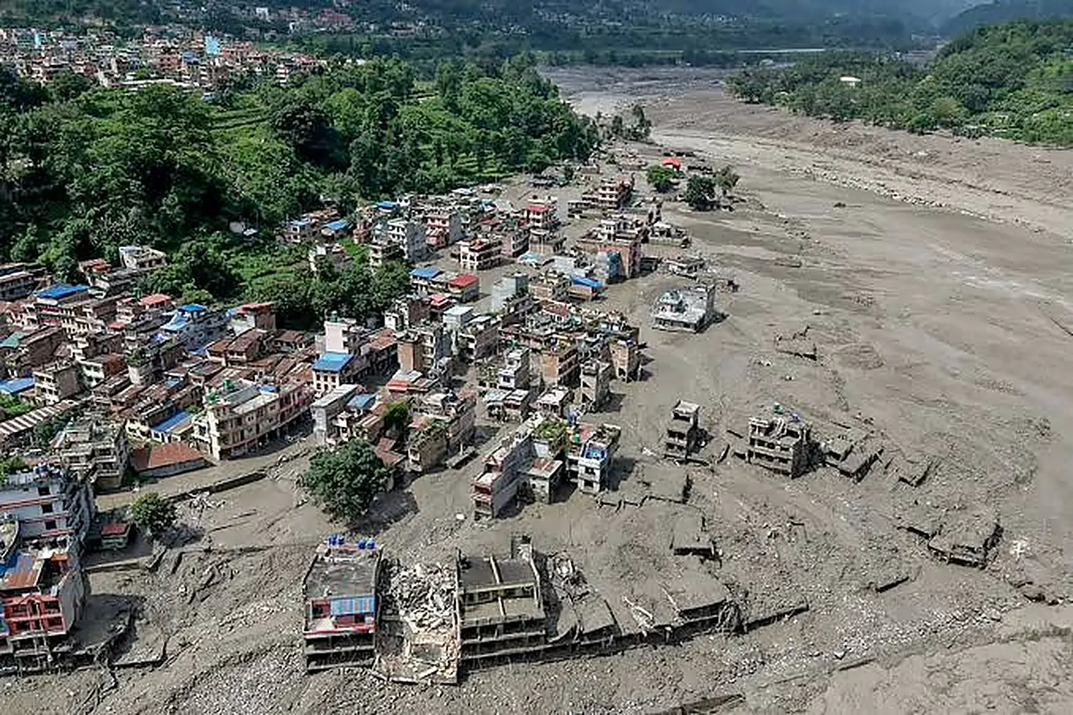 Luchtfoto van een dorp waarvan de huizen aan de rand van een brede grijze modderstroom zijn ingestort