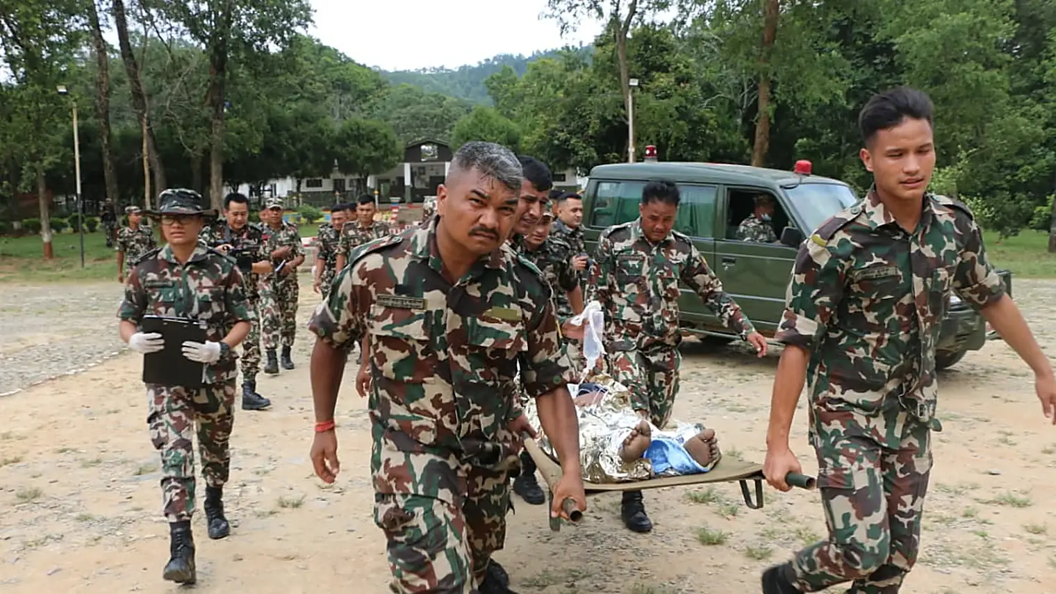 Nepalese militairen dragen een gewonde op een brancard weg bij een legervoertuig