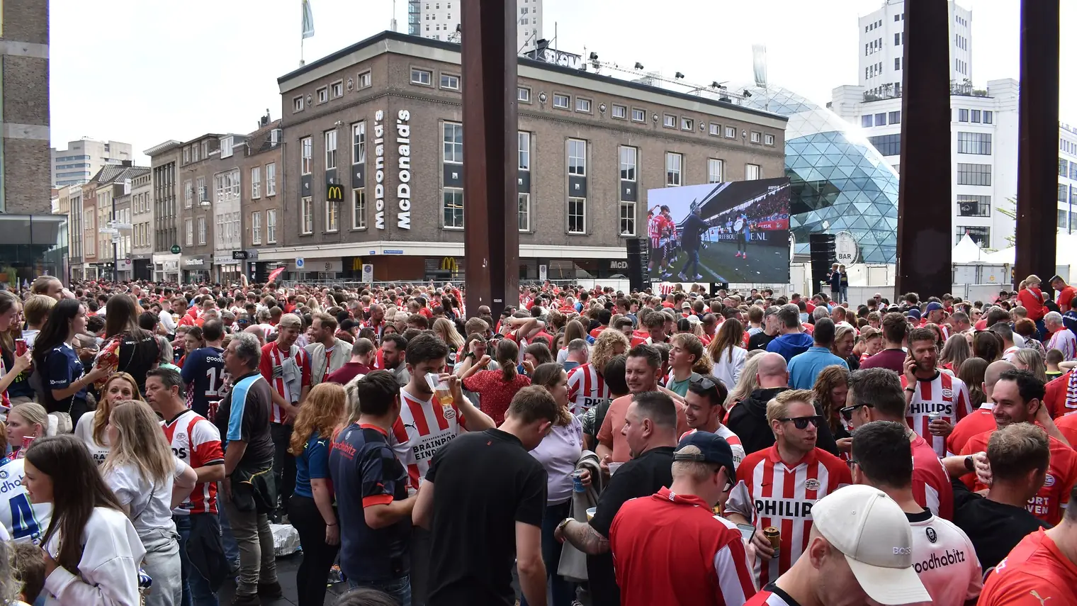Een dichtbevolkt plein in Eindhoven vol PSV-supporters in rood-witte shirts, met de koepel van het Evoluon op de achtergrond
