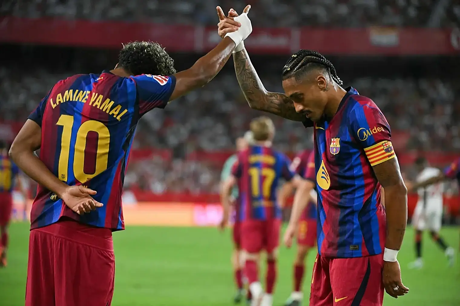 Lamine Yamal en Raphinha slaan een high five na een Barcelona-goal, met het Sevilla-publiek op de achtergrond