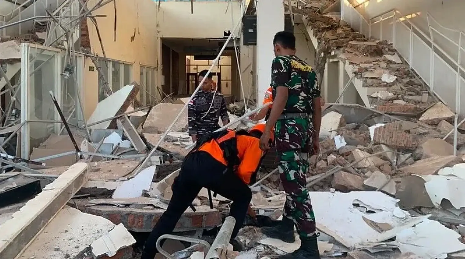 Reddingswerkers van de Indonesische reddingsdienst en militairen zoeken tussen ingestorte muren en puin in een gebouw op Flores