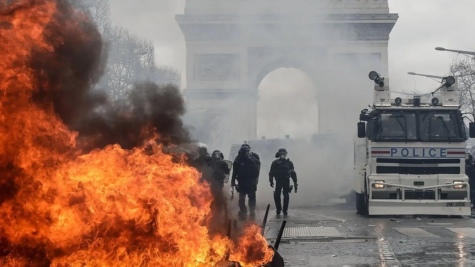 Oproerpolitie en een politiewagen bij brandende barricades voor de Arc de Triomphe in Parijs