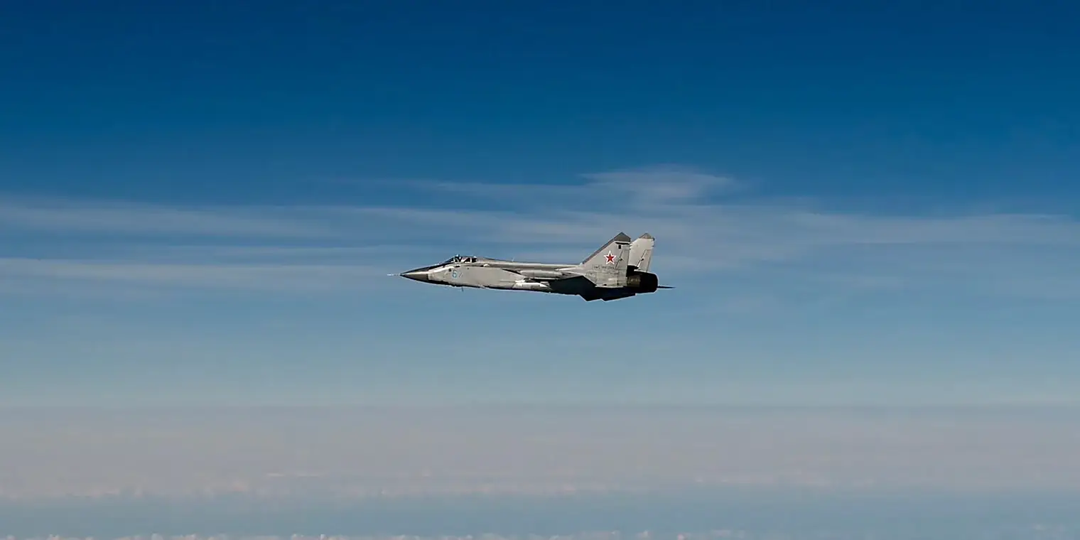 Een Russisch MiG-31-gevechtsvliegtuig van opzij gefotografeerd tegen een blauwe lucht boven zee