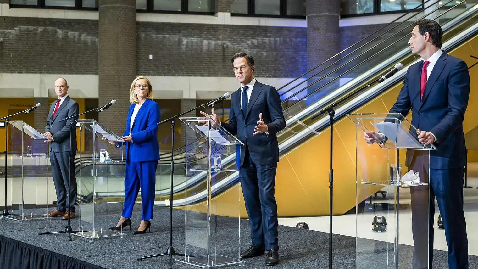 Mark Rutte spreekt achter een doorzichtig spreekgestoelte, met Gert-Jan Segers, Sigrid Kaag en Wopke Hoekstra elk achter een eigen katheder