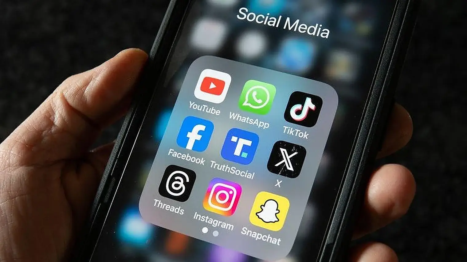 Hand houdt een telefoon vast met een geopende map Social Media met de apps van YouTube, WhatsApp, TikTok, Facebook, X, Threads, Instagram en Snapchat