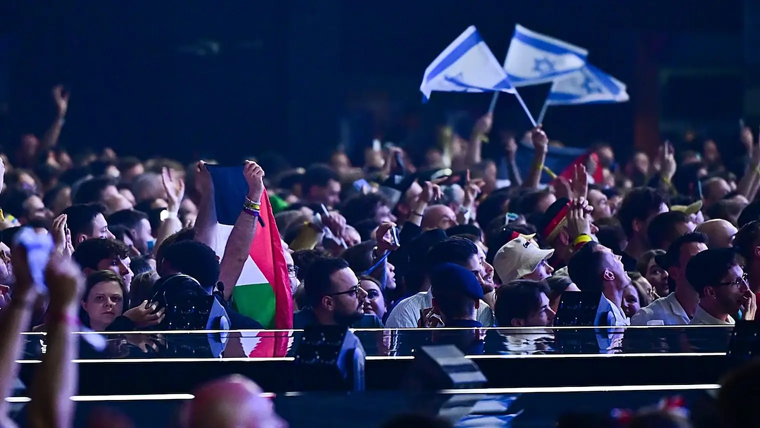 Publiek in een songfestivalzaal waar zowel Israelische vlaggen als een Palestijnse vlag omhoog worden gehouden